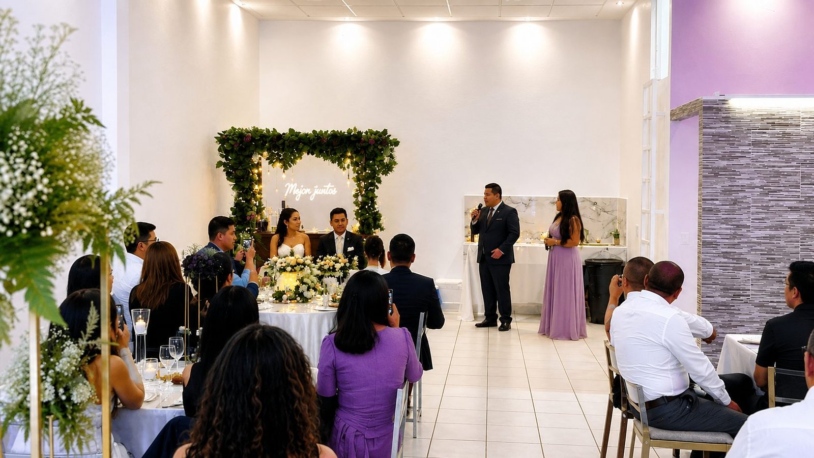 Los novios en la mesa principal bajo un arco de follaje con el letrero «Mejor juntos», mientras los invitados escuchan un brindis