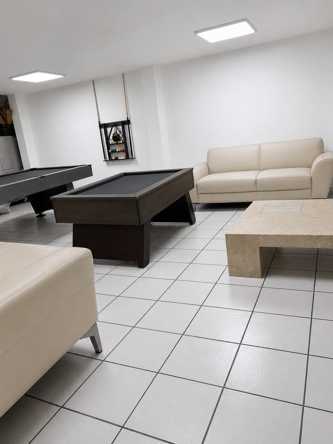 Sala de la zona recreativa, con sillones de piel clara, mesa de centro y dos mesas de billar al fondo